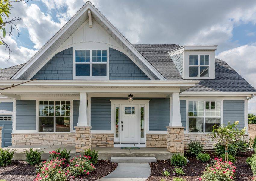 A dark grey paneled single family home with white and stone trim is pictured in center frame and surrounded by plants in an HOA community