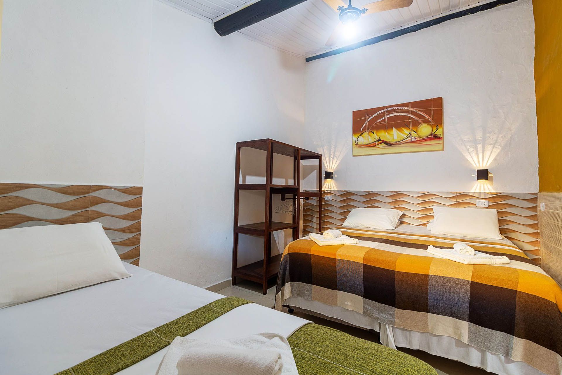 Quarto luminoso com duas camas, paredes brancas, prateleiras de madeira e decoração em tons quentes de laranja.