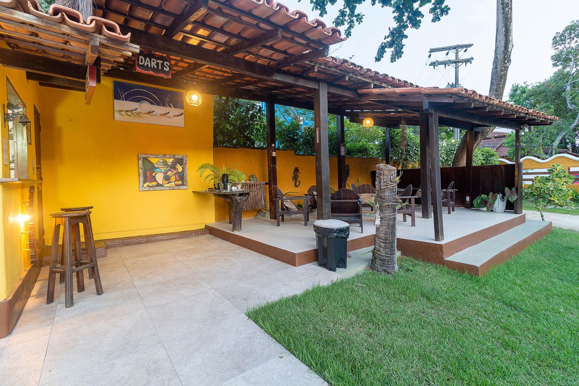 Pátio amarelo ao ar livre com teto de madeira, bancos e gramado verde ao entardecer.