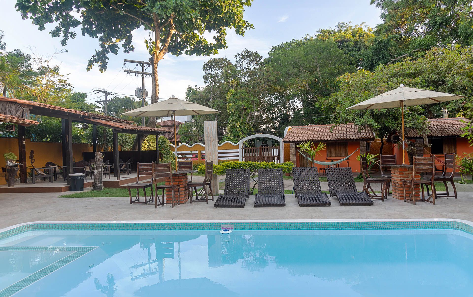 Área de estar à beira da piscina com cadeiras, guarda-sóis e cabanas em um resort tropical.