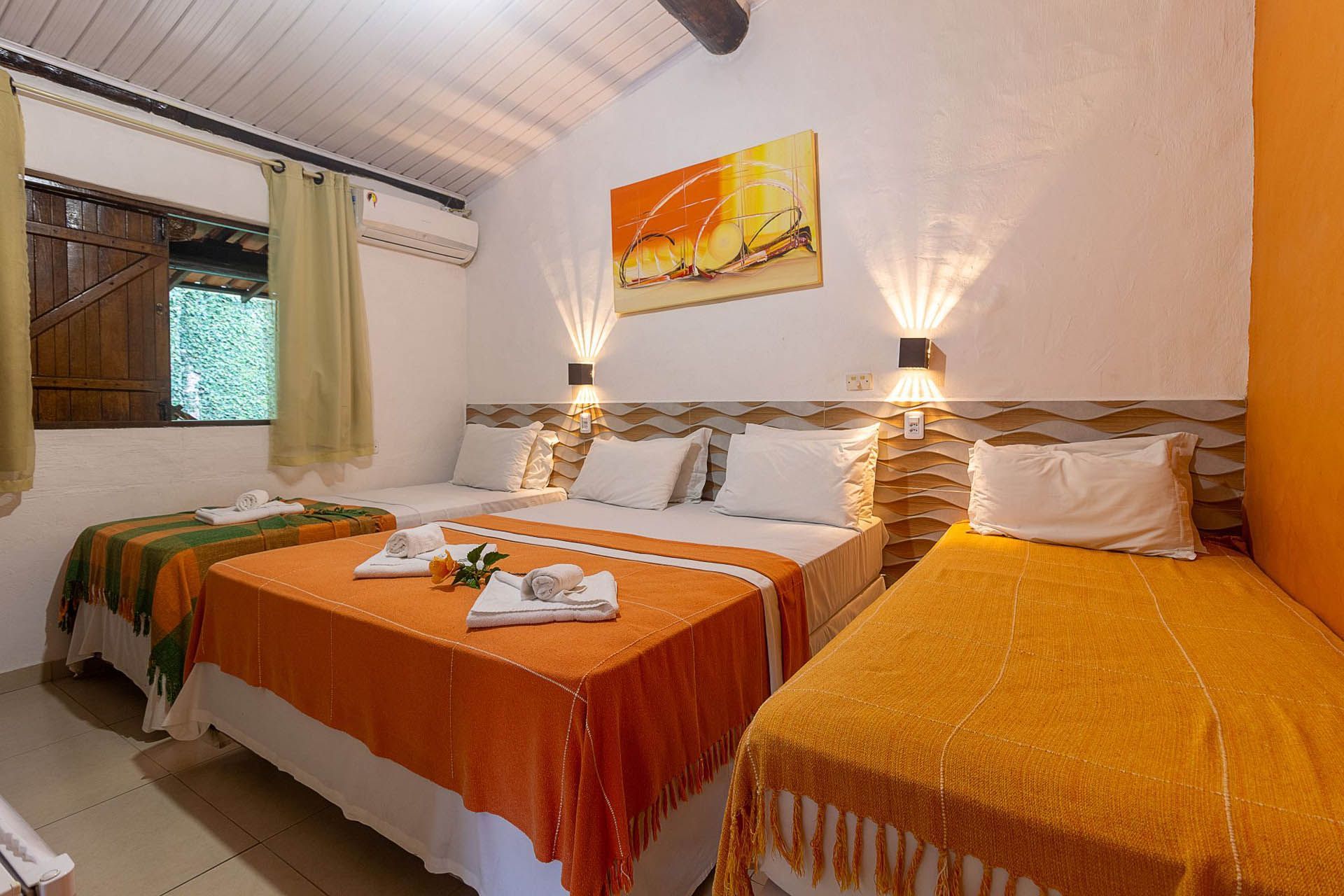 Quarto aconchegante com duas camas de solteiro, roupa de cama laranja, abajures e um pequeno quadro na parede.