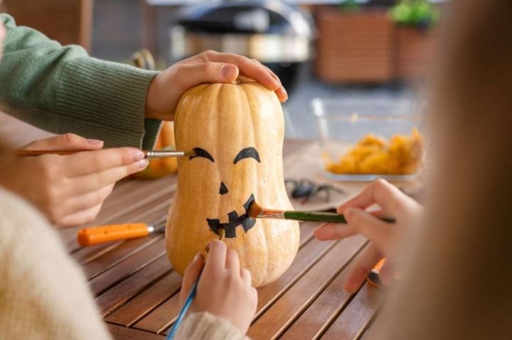 A group of people are painting a pumpkin with a brush.