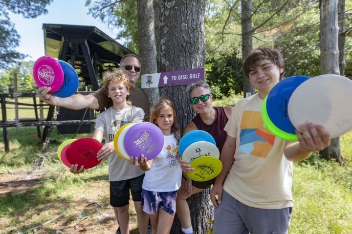 A group of people are holding frisbees in front of a tree.