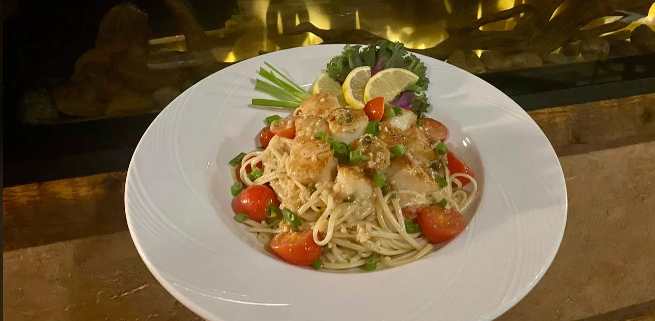 A white plate topped with noodles , shrimp and tomatoes.