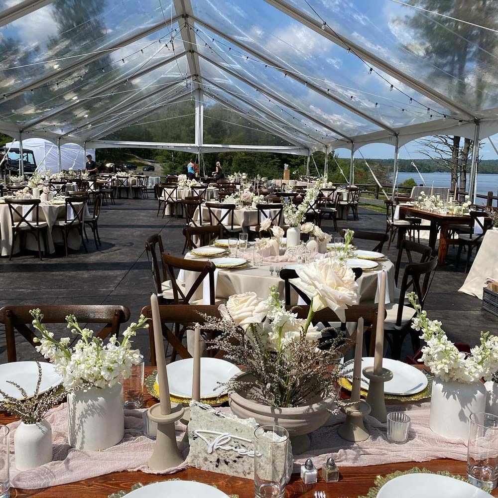 A clear tent with tables and chairs set up for a wedding reception.