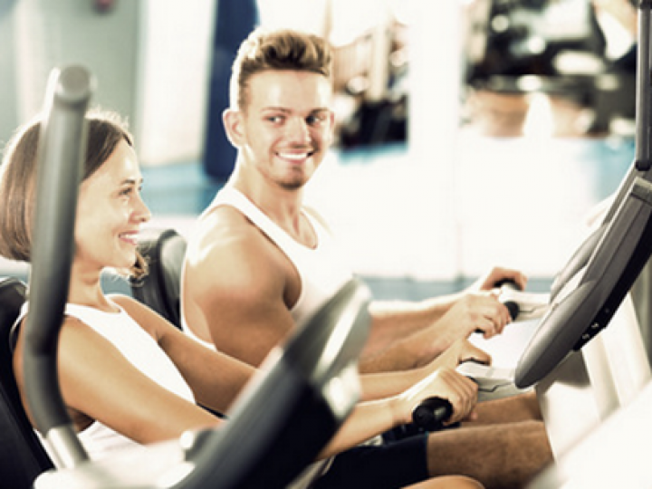 A man and a woman are riding exercise bikes in a gym.