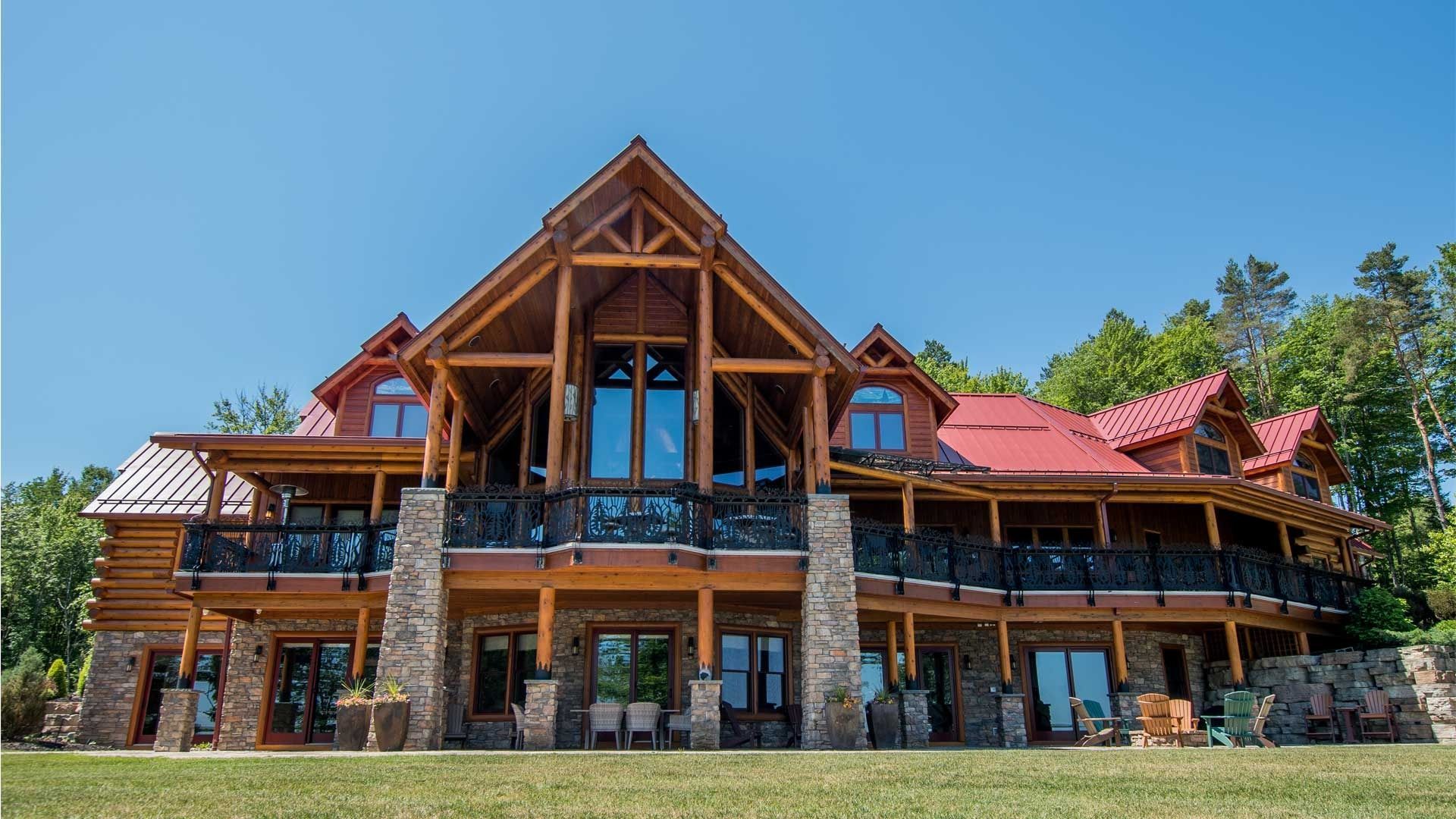 A large log cabin with a red roof is sitting on top of a lush green field.