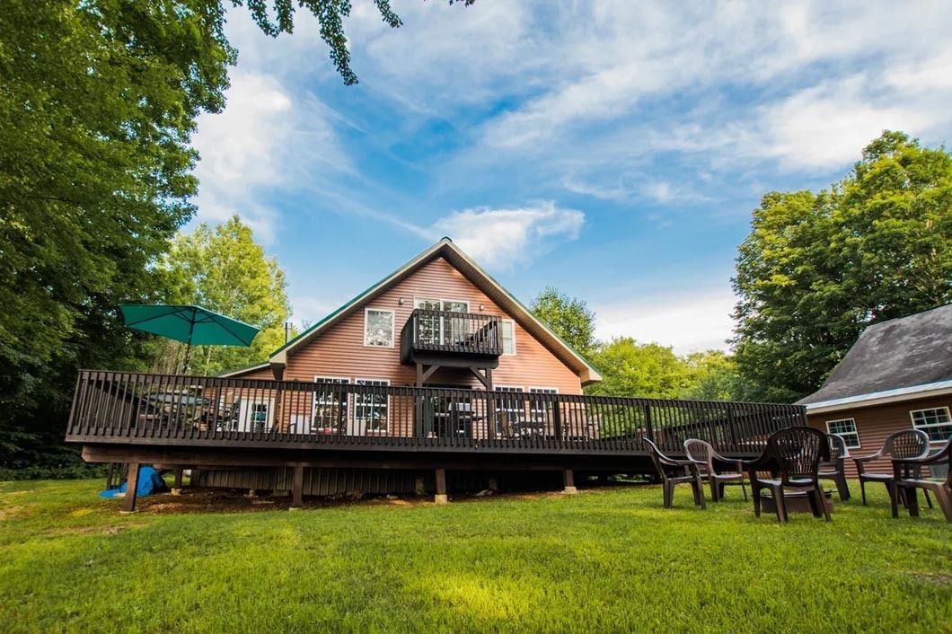 A large house with a large deck in the backyard surrounded by trees.