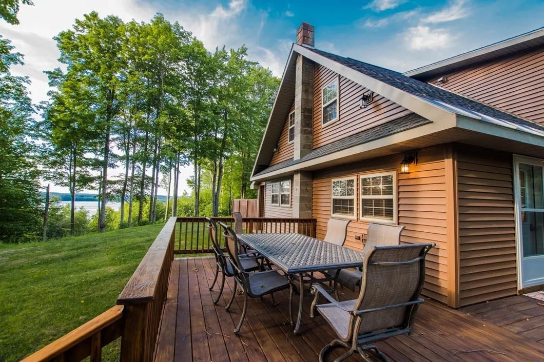 A large wooden deck with a table and chairs in front of a house.