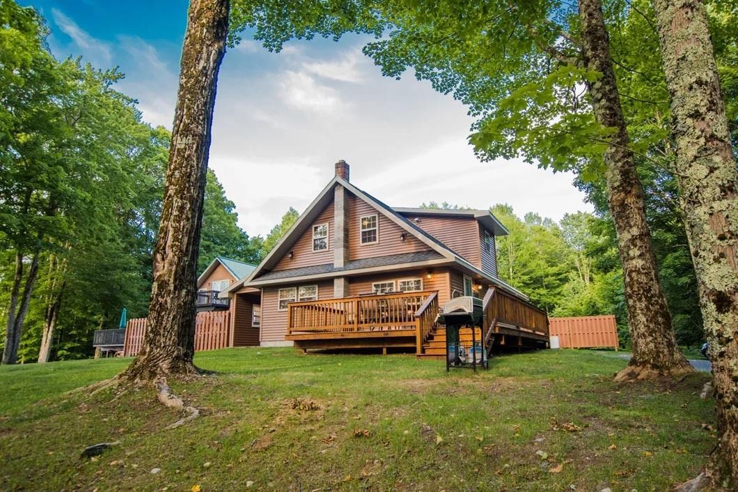 A large house with a large deck is surrounded by trees.