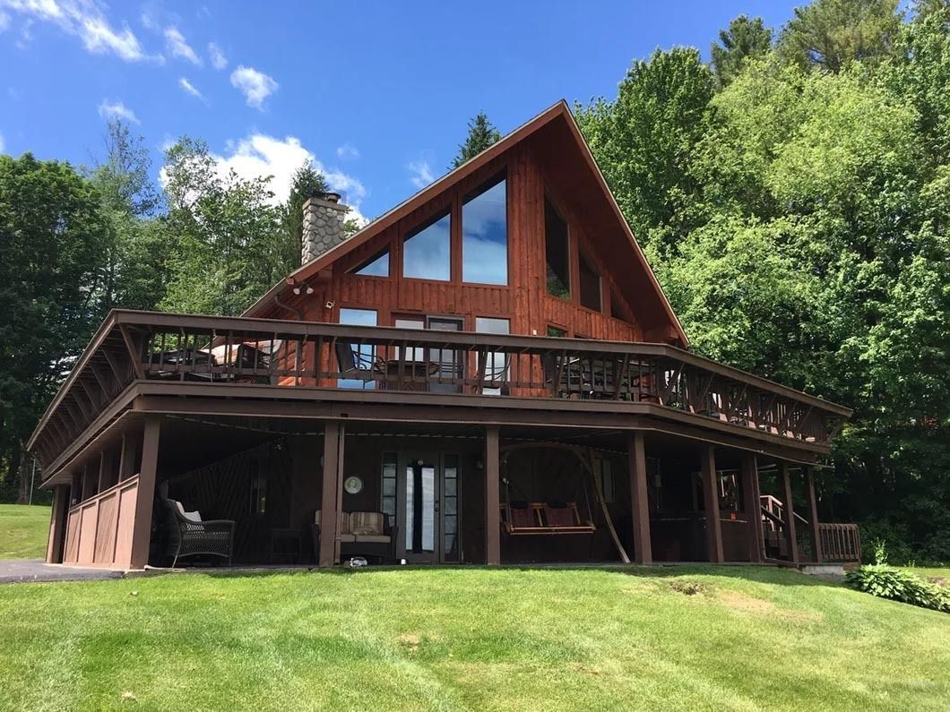 A large wooden house with a large deck is surrounded by trees.