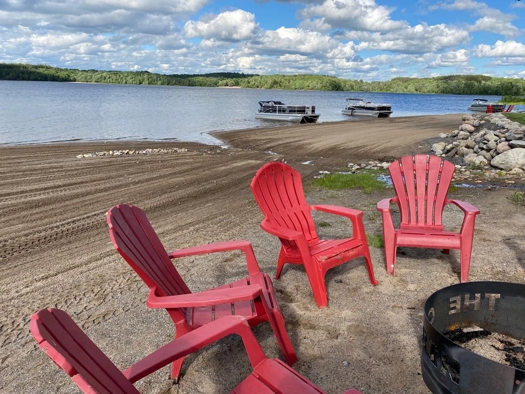 A group of red chairs are sitting on a sandy beach near a lake.