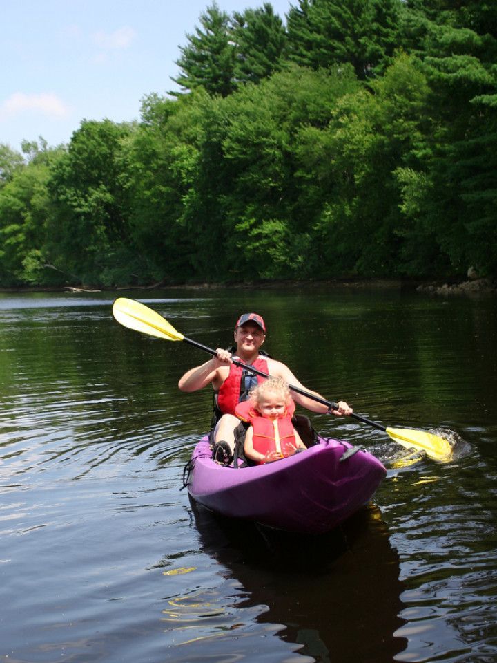 A woman and a child are paddling a purple kayak on a lake.
