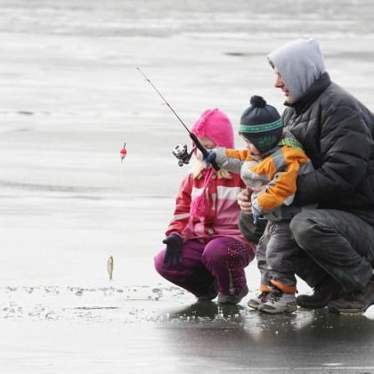 A man and two children are fishing on a frozen lake