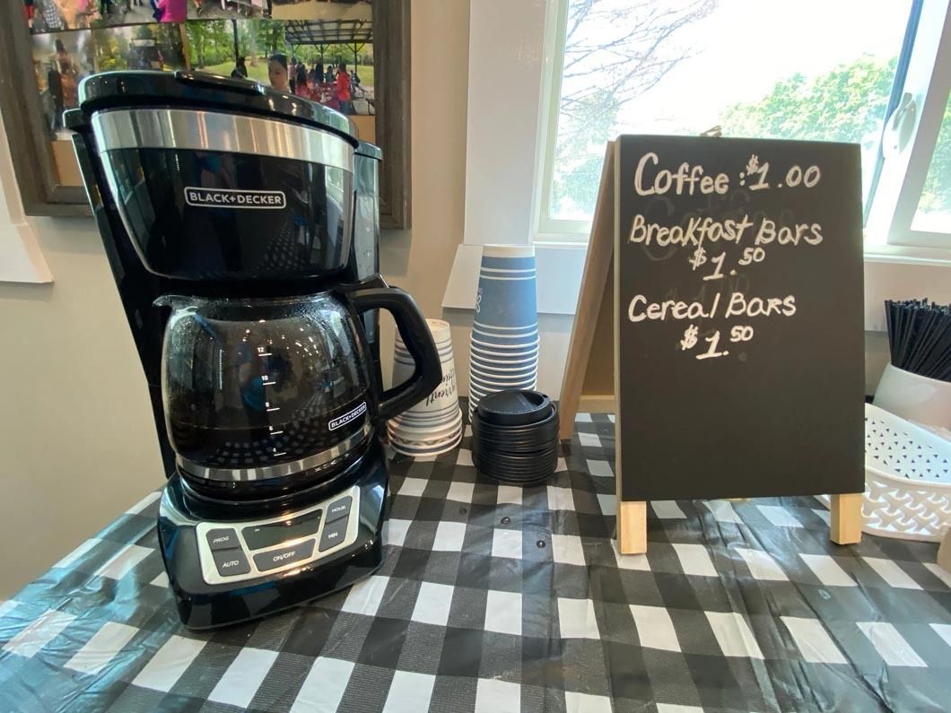 A coffee maker is sitting on a table next to a chalkboard.