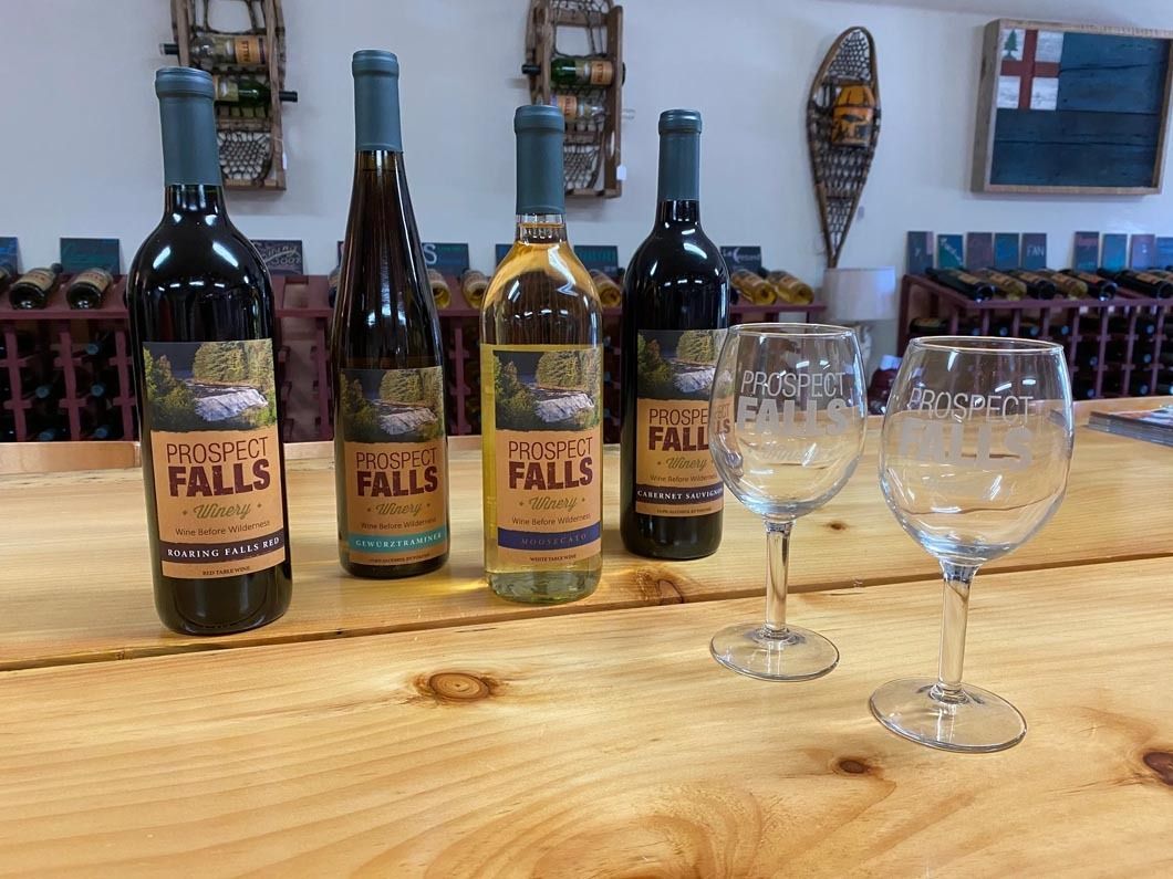Four bottles of wine and two wine glasses are sitting on a wooden table.