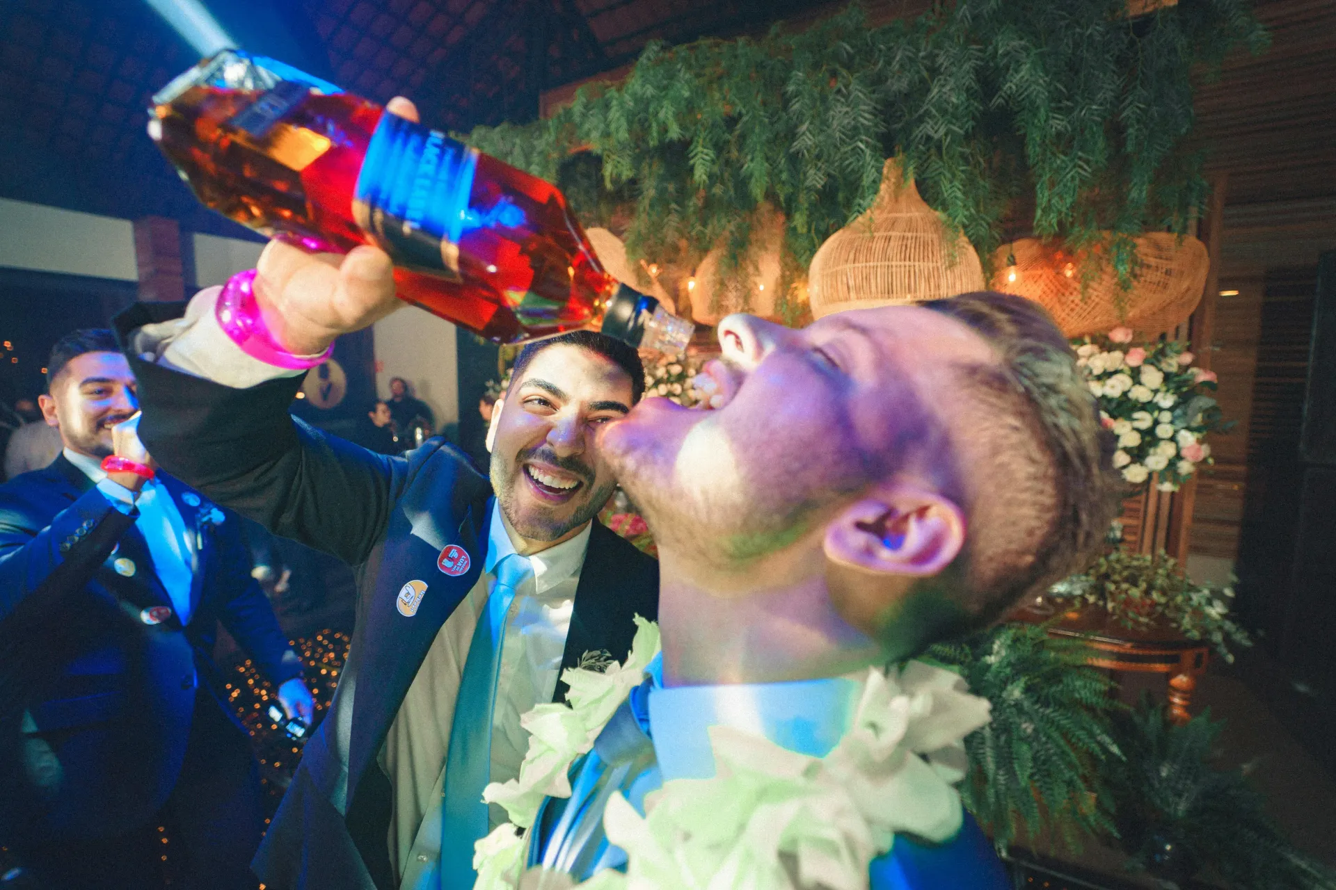 Man at bachelor party pouring rum in another mans mouth.