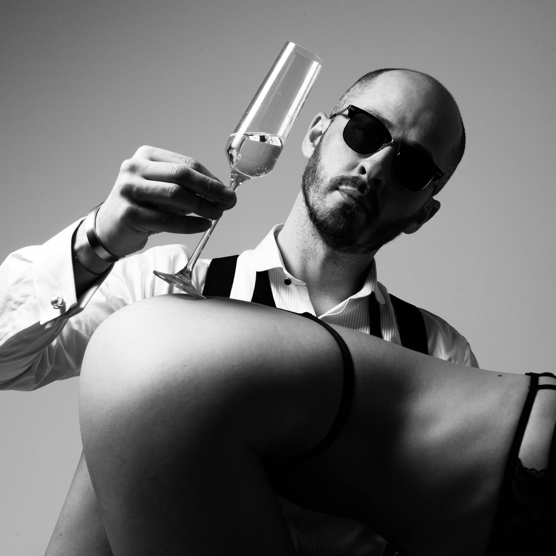 Man wearing sunglasses holds a glass of champagne on a woman’s lower back