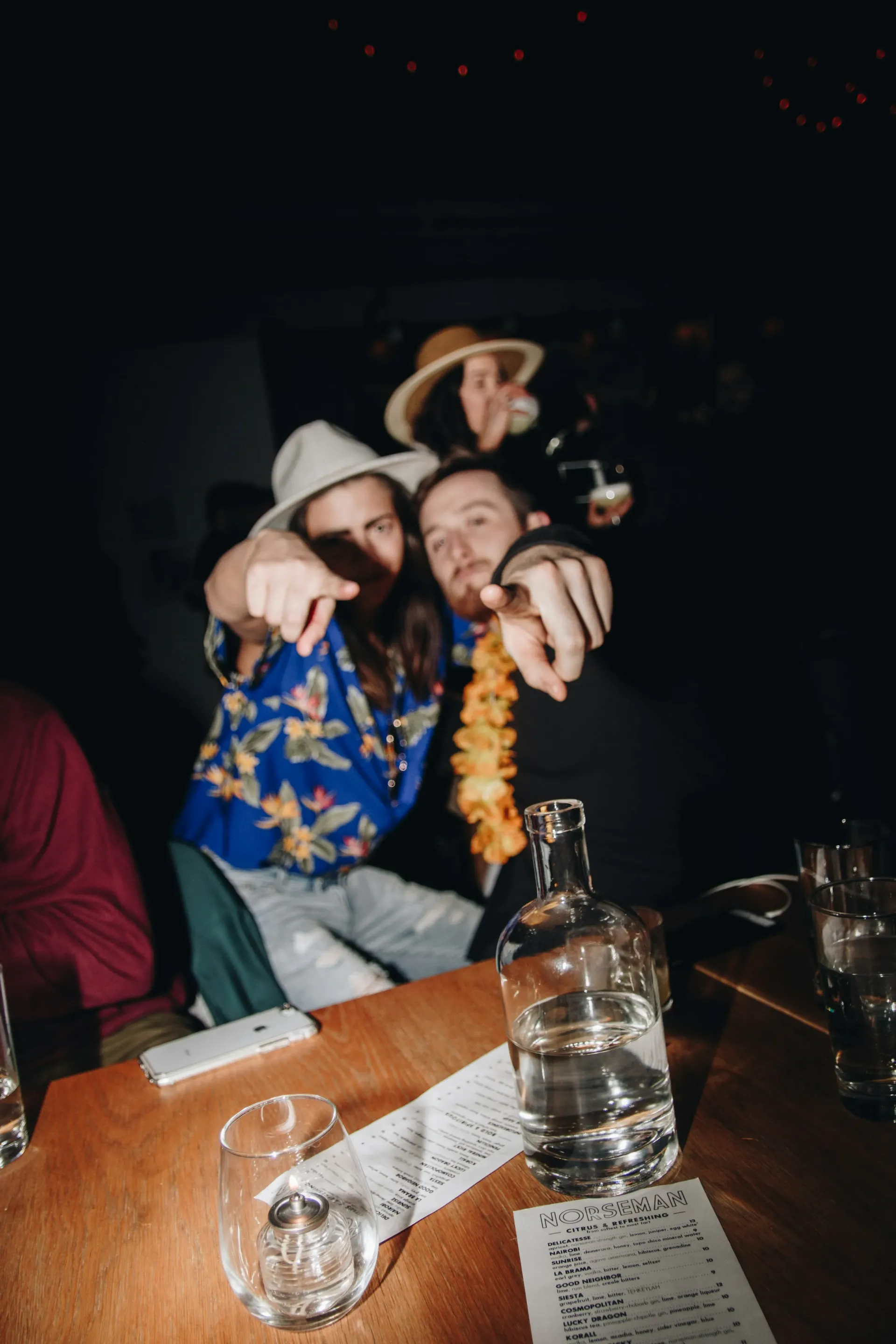 Two people wearing Hawaiian attire point at the viewer celebrating a bachelor party.