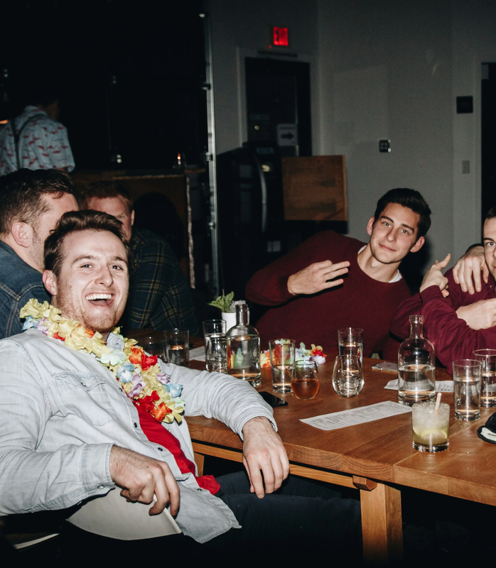 Friends at a bachelor party smiling, sharing drinks at a table.