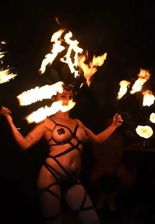 Fire performer twirls fire fans wearing a black strappy costume.