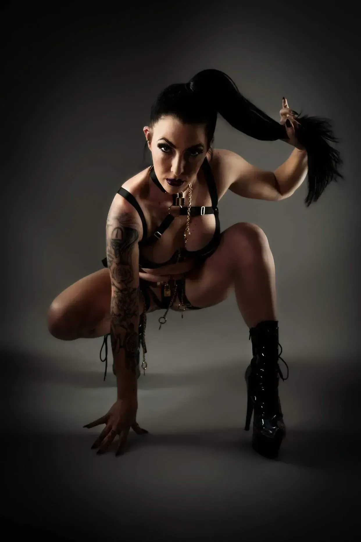 Fire dancer in leather harness and boots, crouched with ponytail raised.