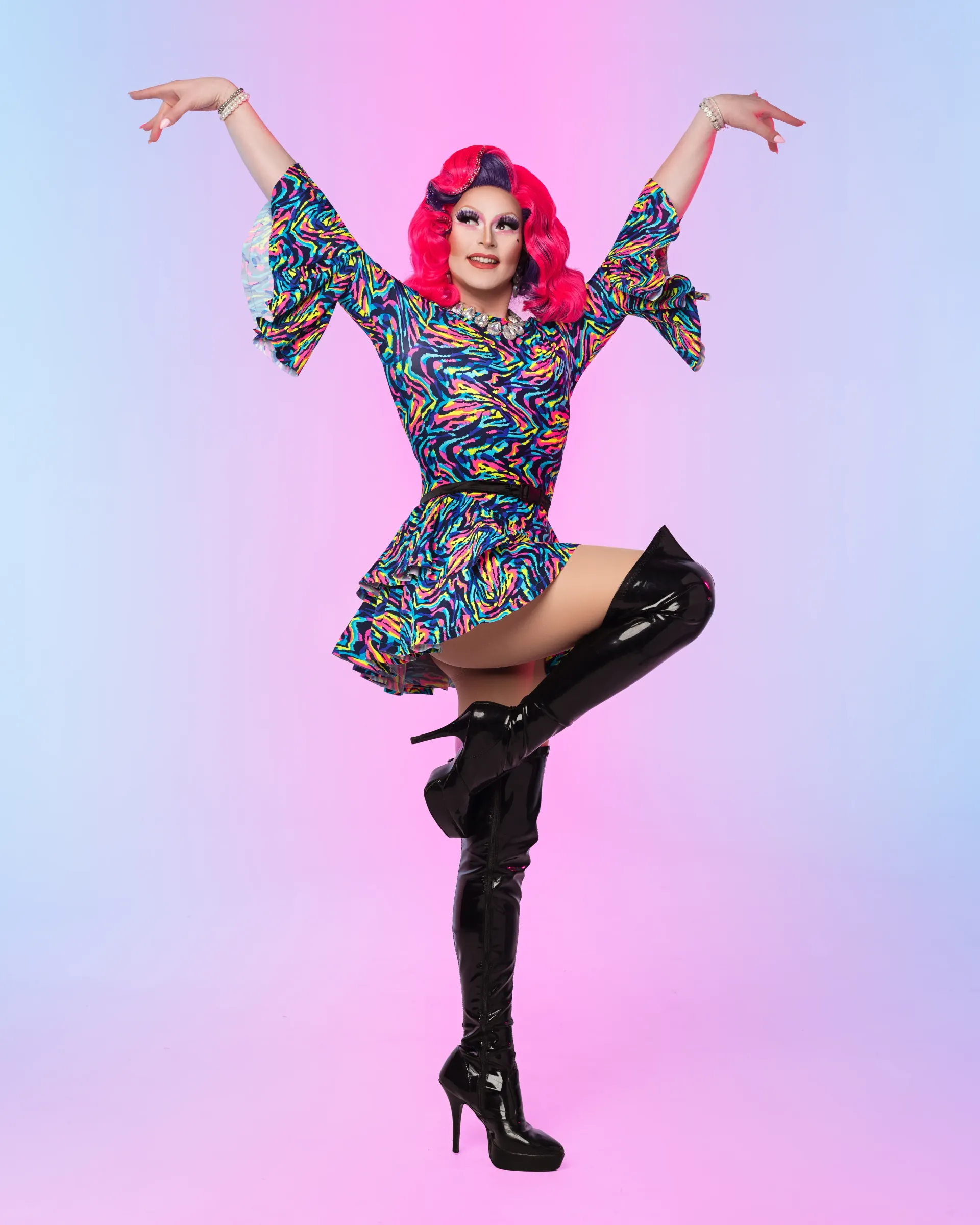 Drag performer posing, wearing floral dress and black thigh high boots.