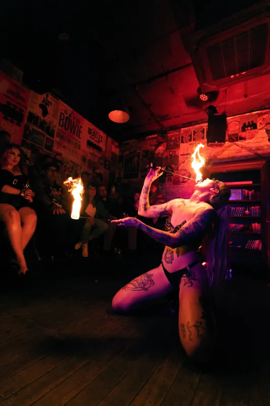 Fire dancer eating fire for an audience at dim lit venue.