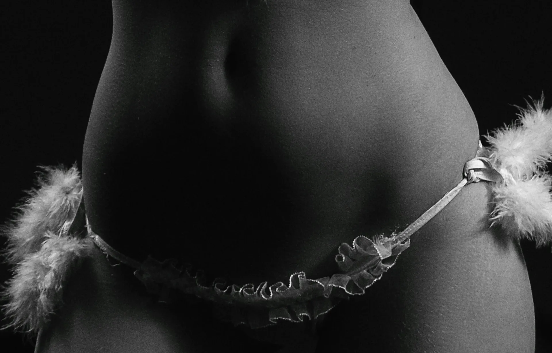 Black-and-white close-up of a torso wearing a decorative chain with feather accents around the hips