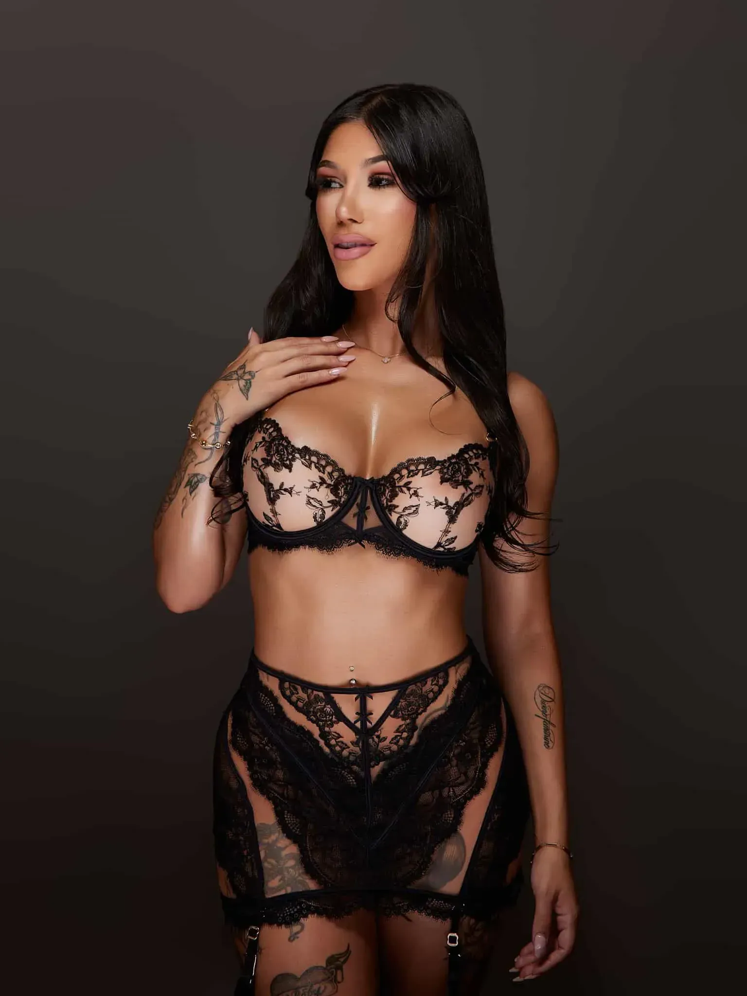 Stripper in black lace lingerie posing against a dark background.