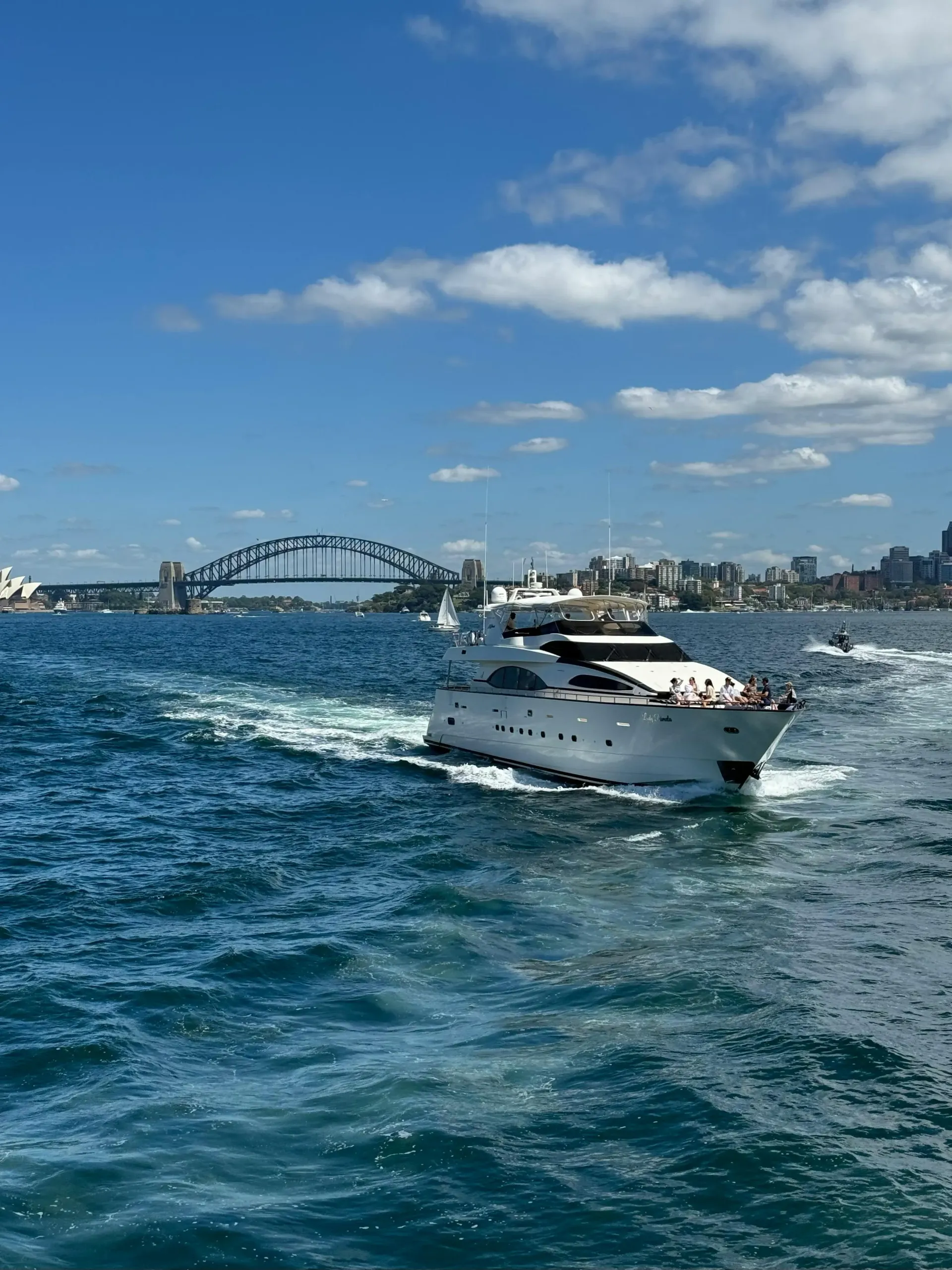 Yacht sailing on blue water in Sydney Harbour, with the Harbour Bridge and city skyline under a blue sky.