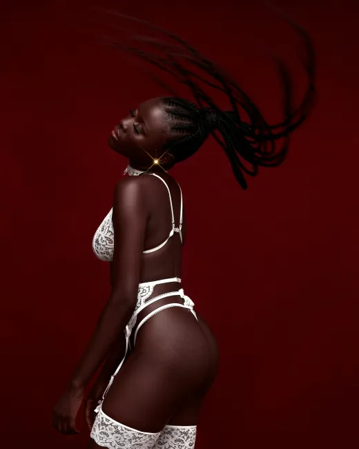 Female adult entertainer wearing white lingerie on red background.