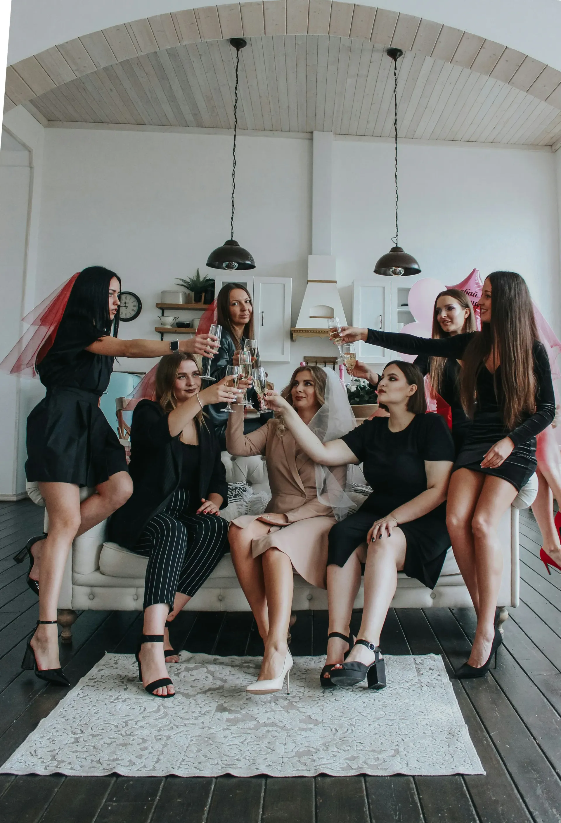 Women sitting on a couch cheering champagne glasses celebrating a hens party.