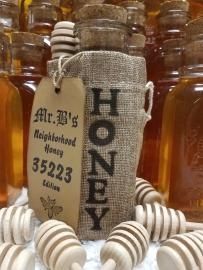 Honey bottle with burlap wrap labeled “HONEY,” surrounded by small striped honey dippers.
