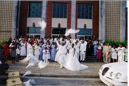 Wedding party outside a church, with a bride in white and guests gathered on the steps