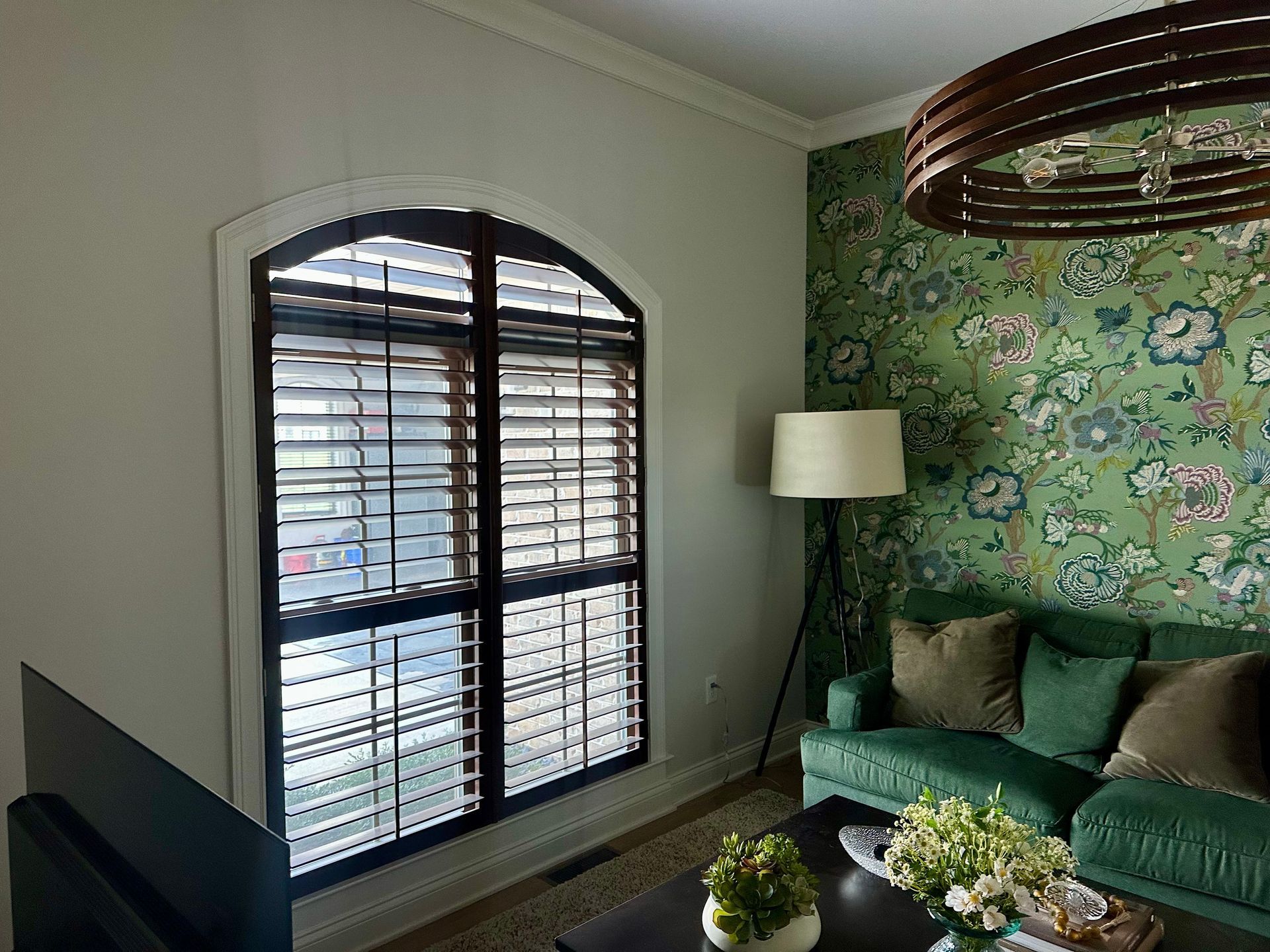 Living room with arched window, green sofa, floral wallpaper, and brown chandelier.