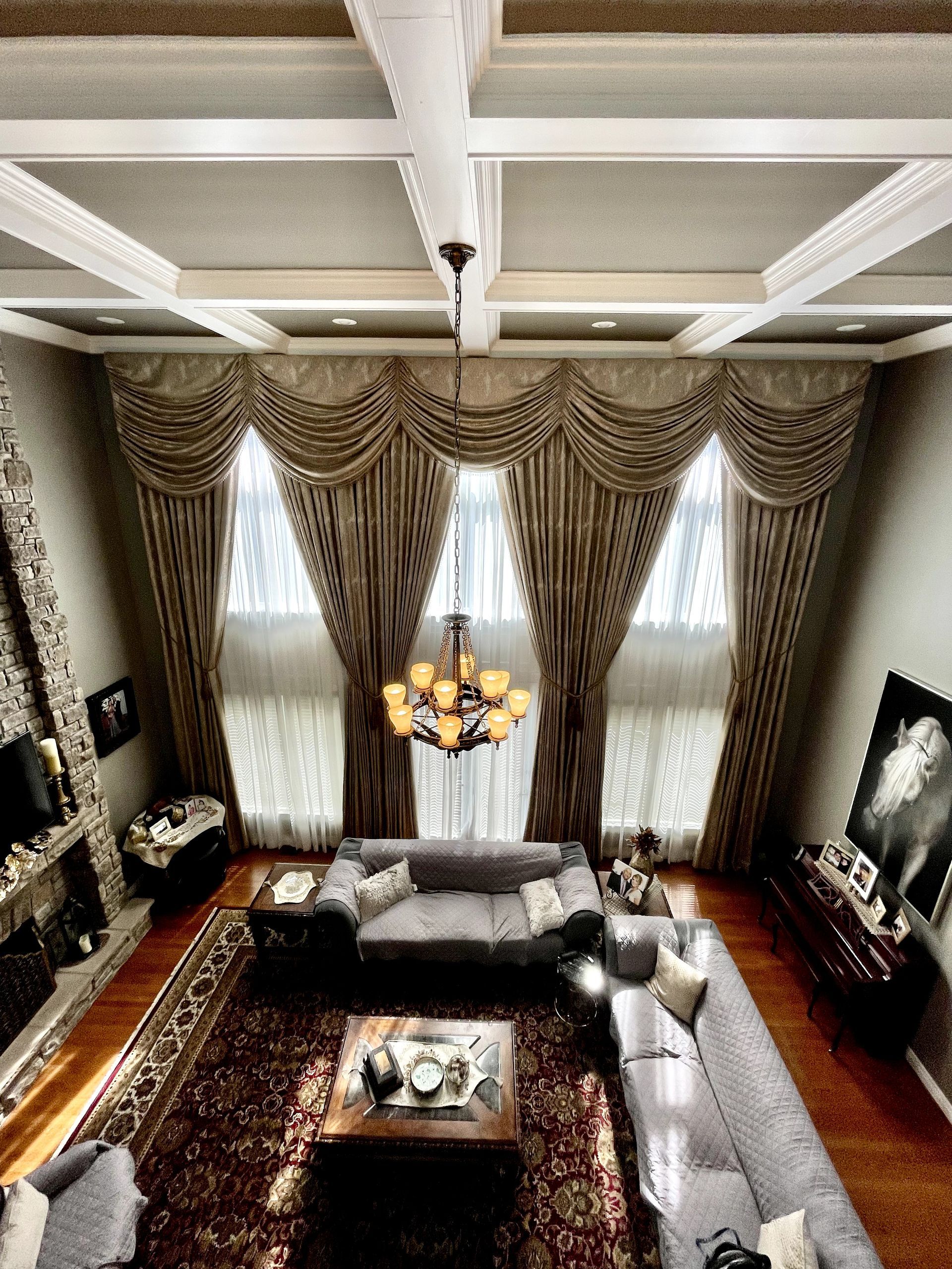 High-angle view of a luxurious living room with ornate draped curtains, large rug, and sectional sofa.