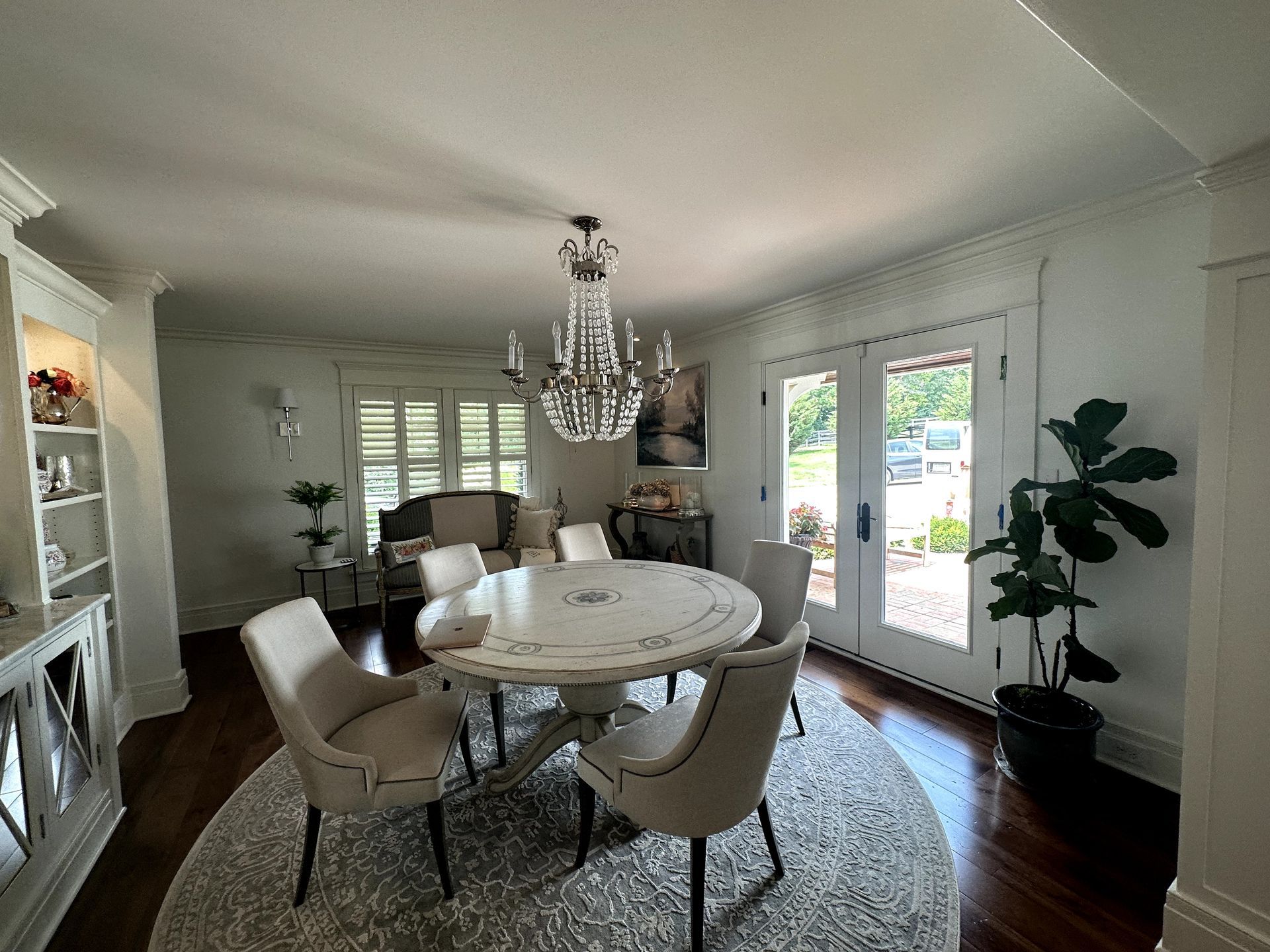 Elegant dining room with round table, chandelier, chairs, and French doors.