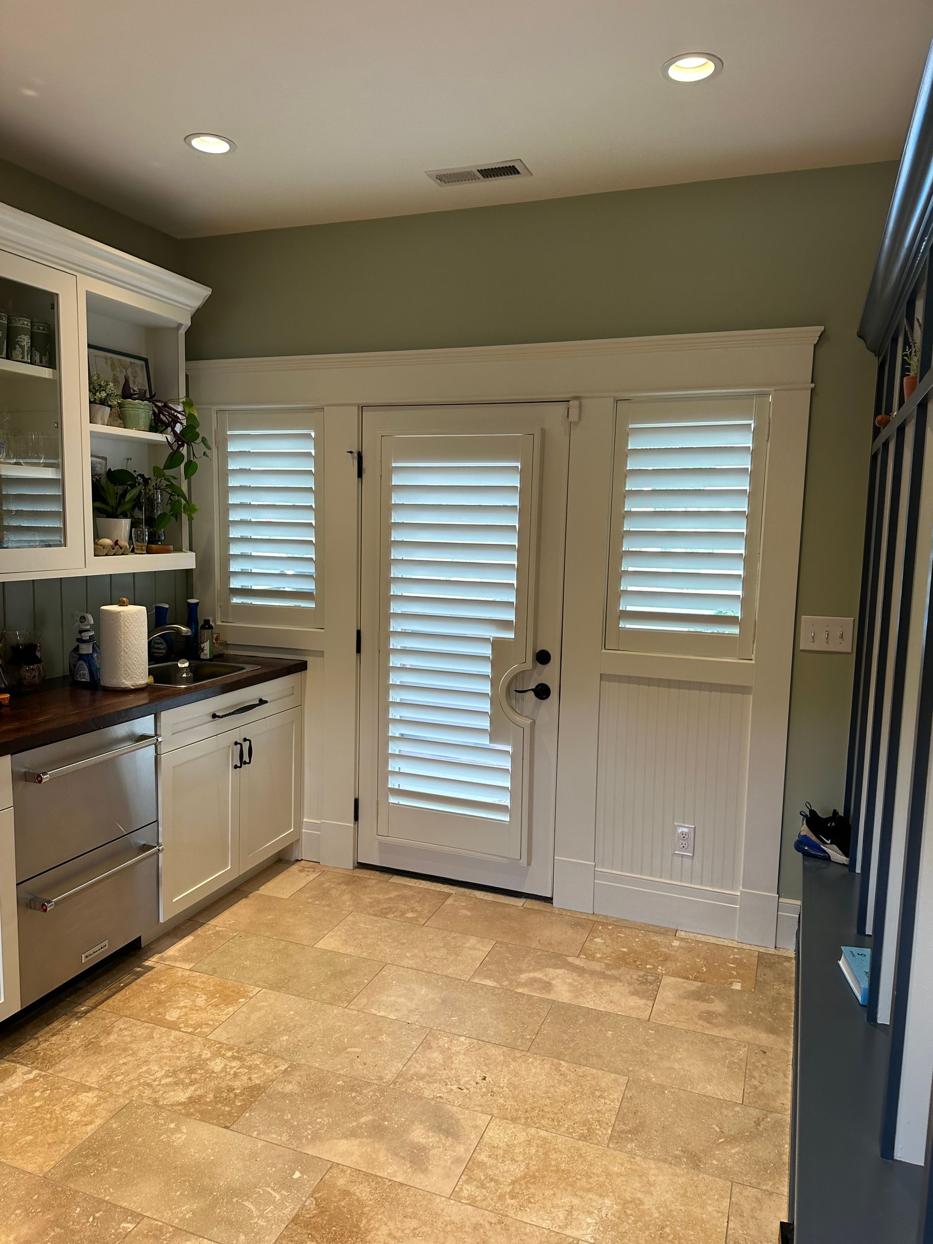 A kitchen with white cabinets, stainless steel appliances, and white shuttered doors.