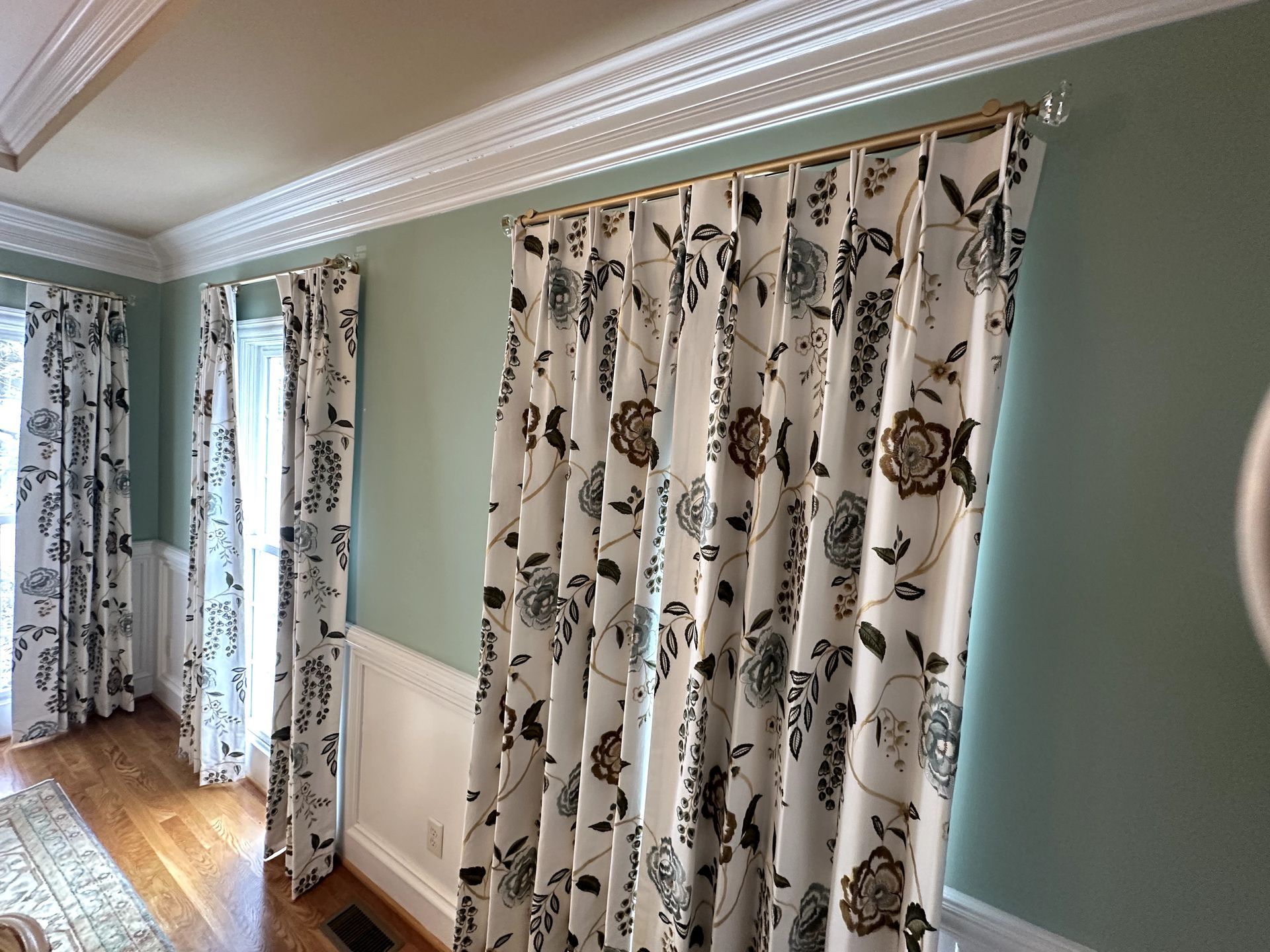 Room with floral print curtains, gold rod, and decorative molding against a light green wall.