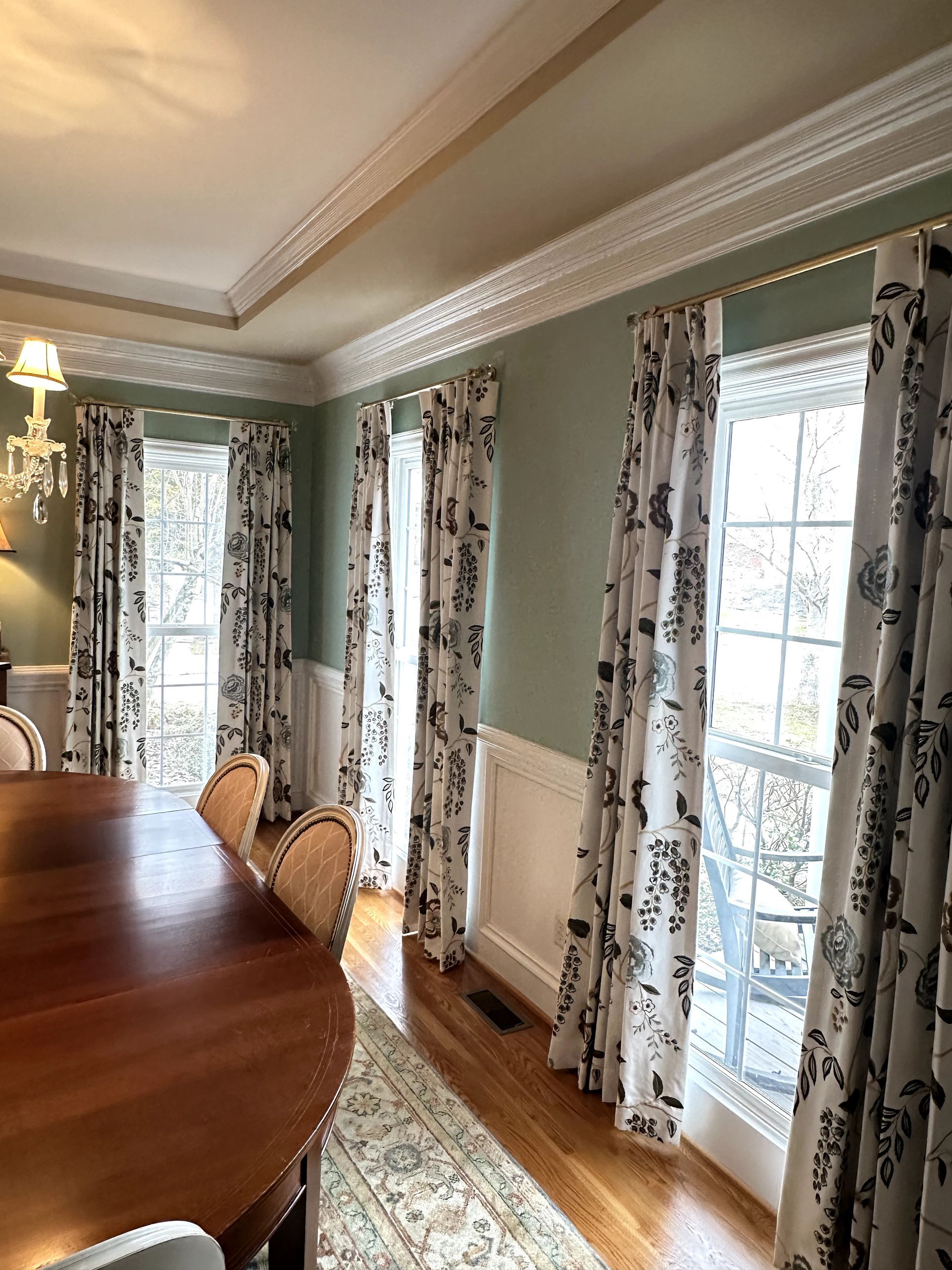 Window with white frame, sheer shades, and patterned, floor-length curtains. Green trees visible outside.
