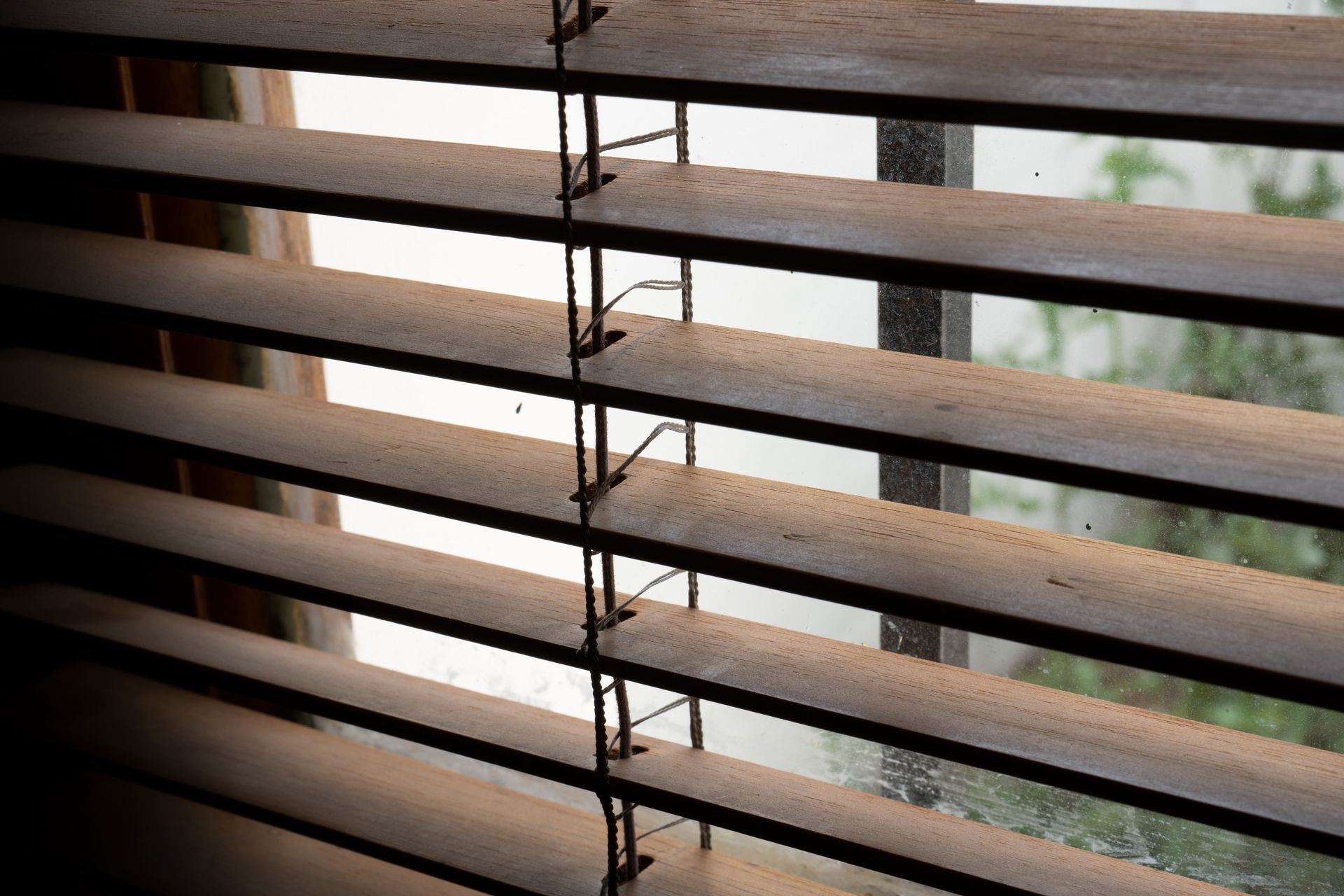 Close-up of horizontal window blinds with daylight and a blurred outdoor view beyond