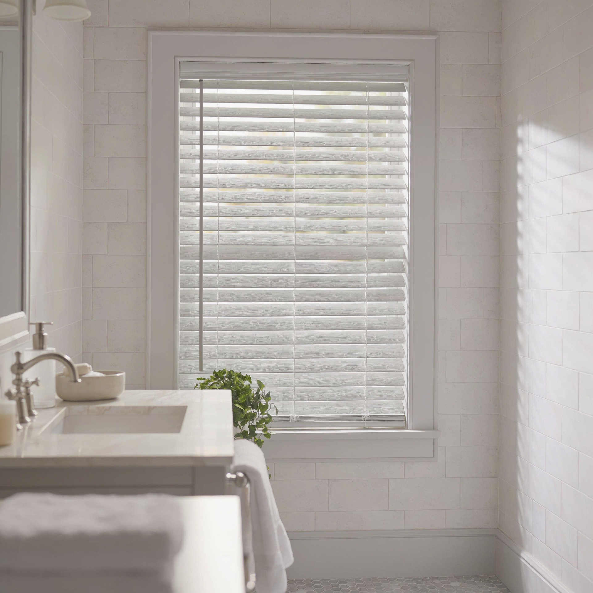 Bright white bathroom with a sink, tiled walls, and a window covered by faux wood blinds.