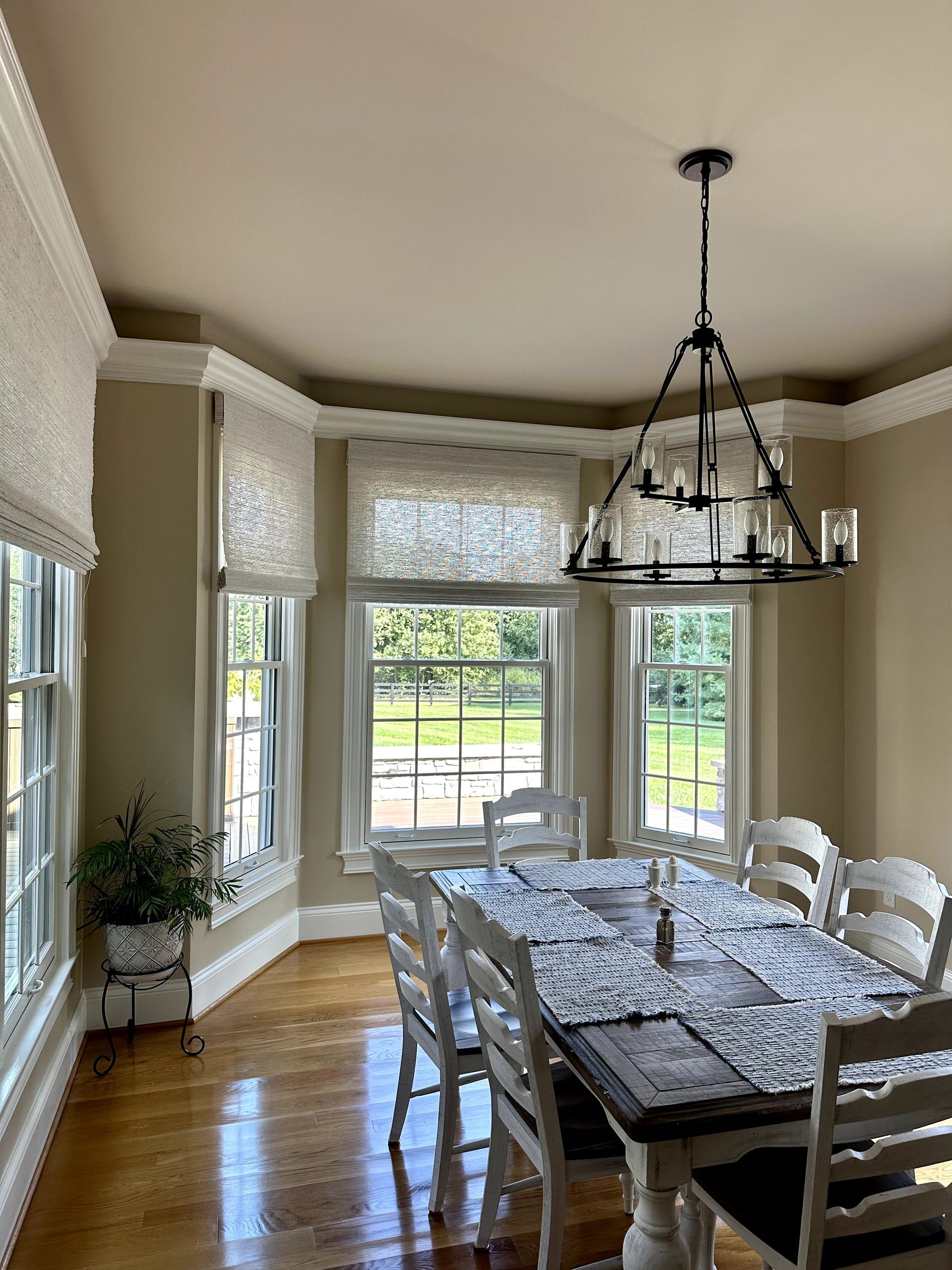 Dining room with wood floor, windows, and a table set for dining with chairs, a light fixture hangs overhead.