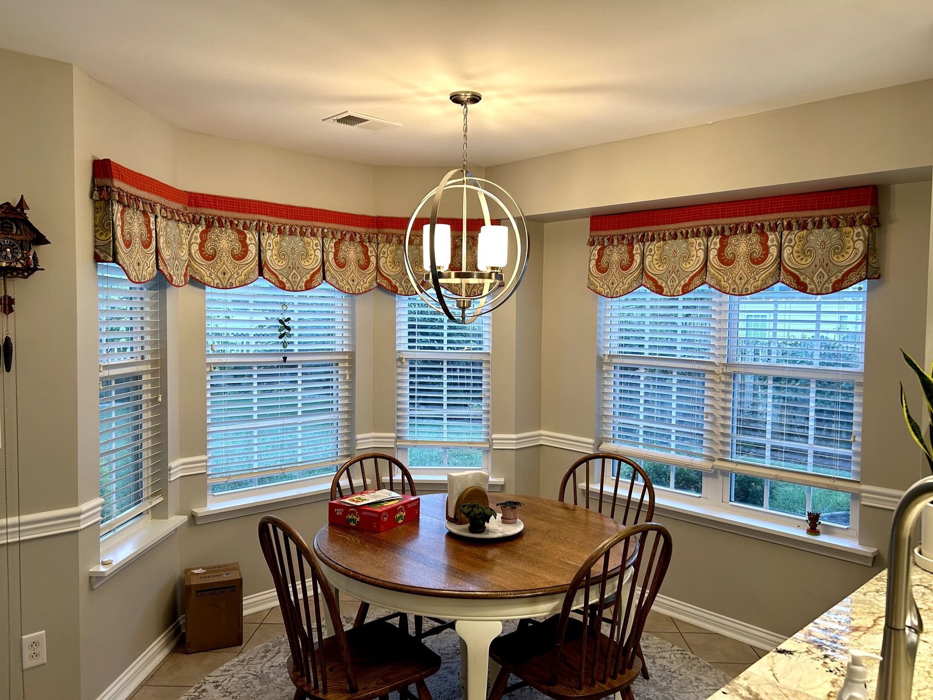 Dining area with round table, chairs, and patterned valances over windows.