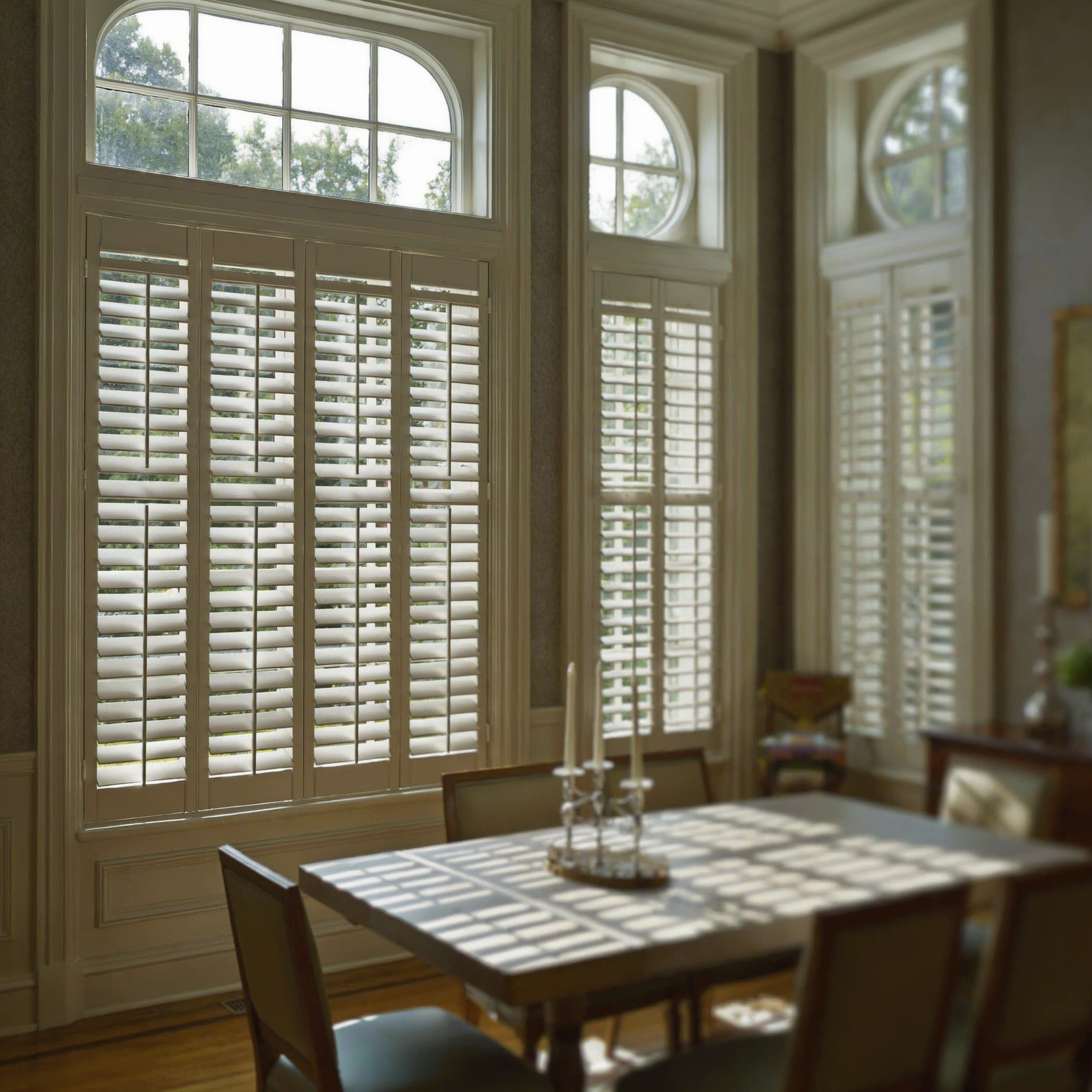 Sunlit dining room with tall windows, white shutters, and a wooden table with chairs
