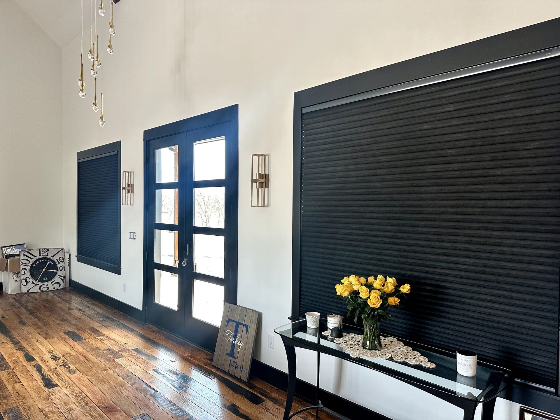 Interior with black window coverings, door, and trim. Yellow flowers on a table.