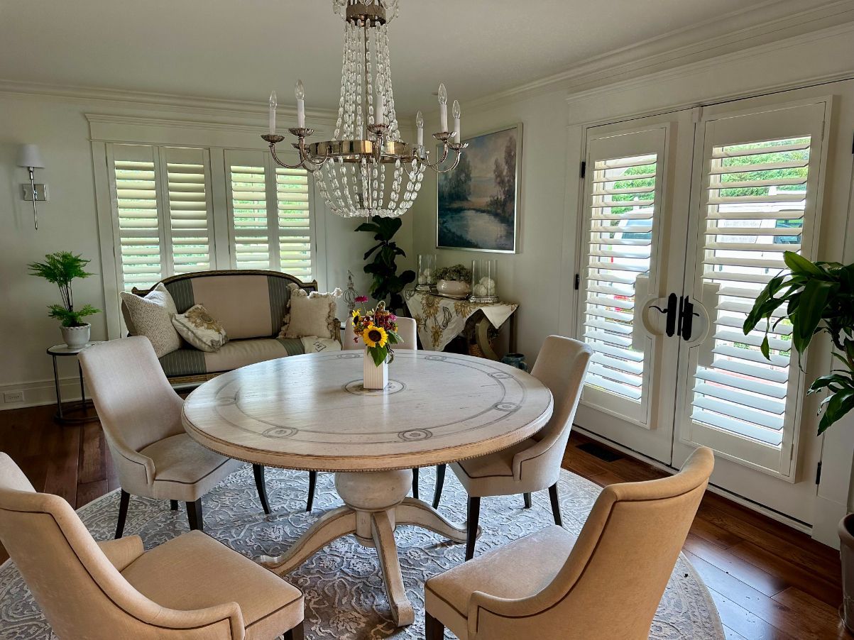 Elegant dining room with round table, beige chairs, chandelier, sofa, and bright French doors