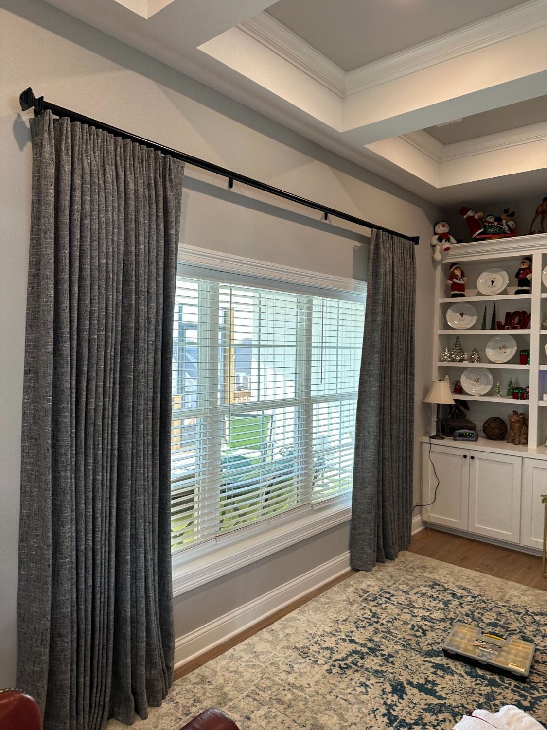 Living room with large window, gray curtains, built-in white shelves, and patterned rug