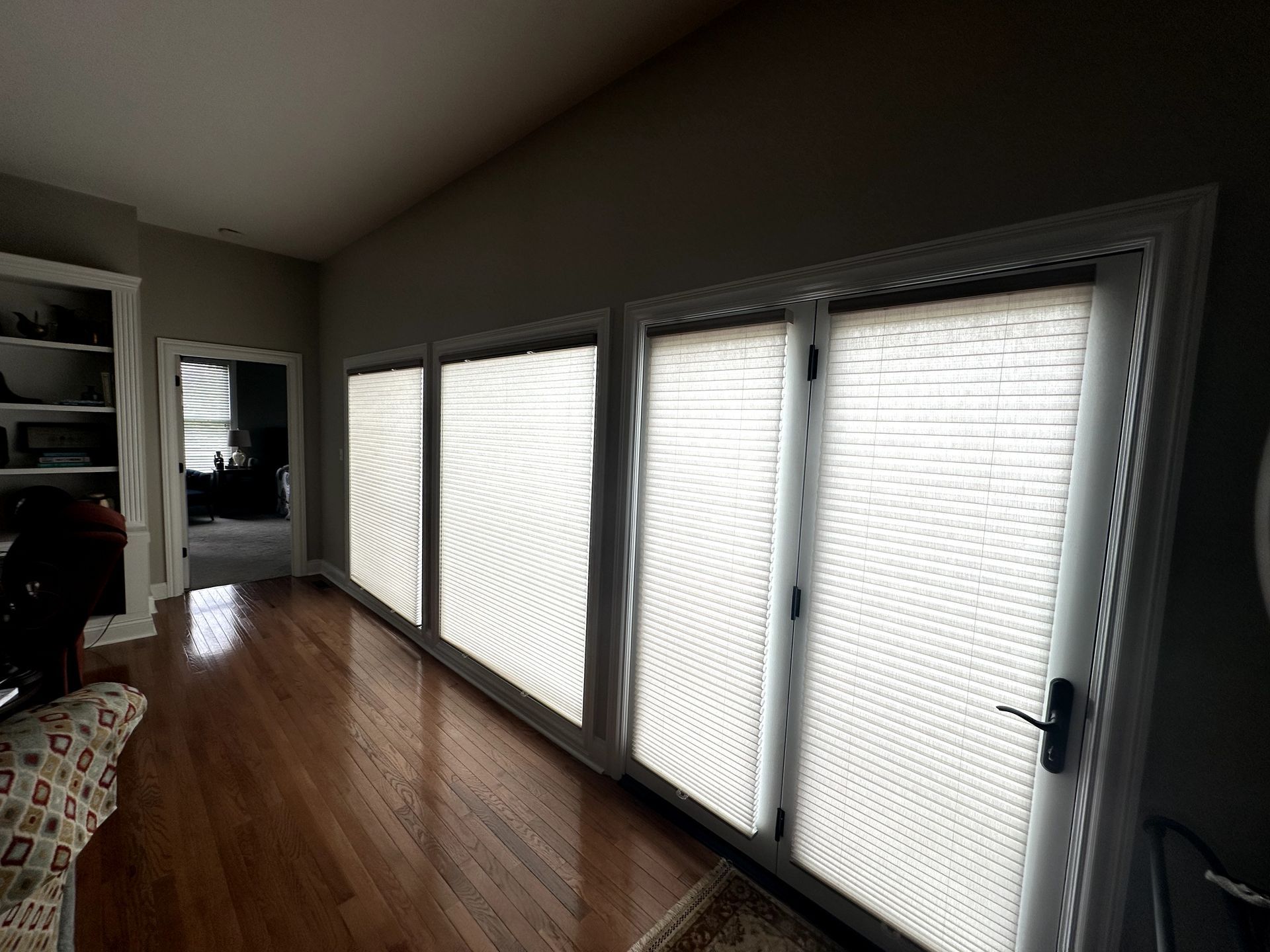 Long, wide room with wood floors and three glass doors, each with white blinds.
